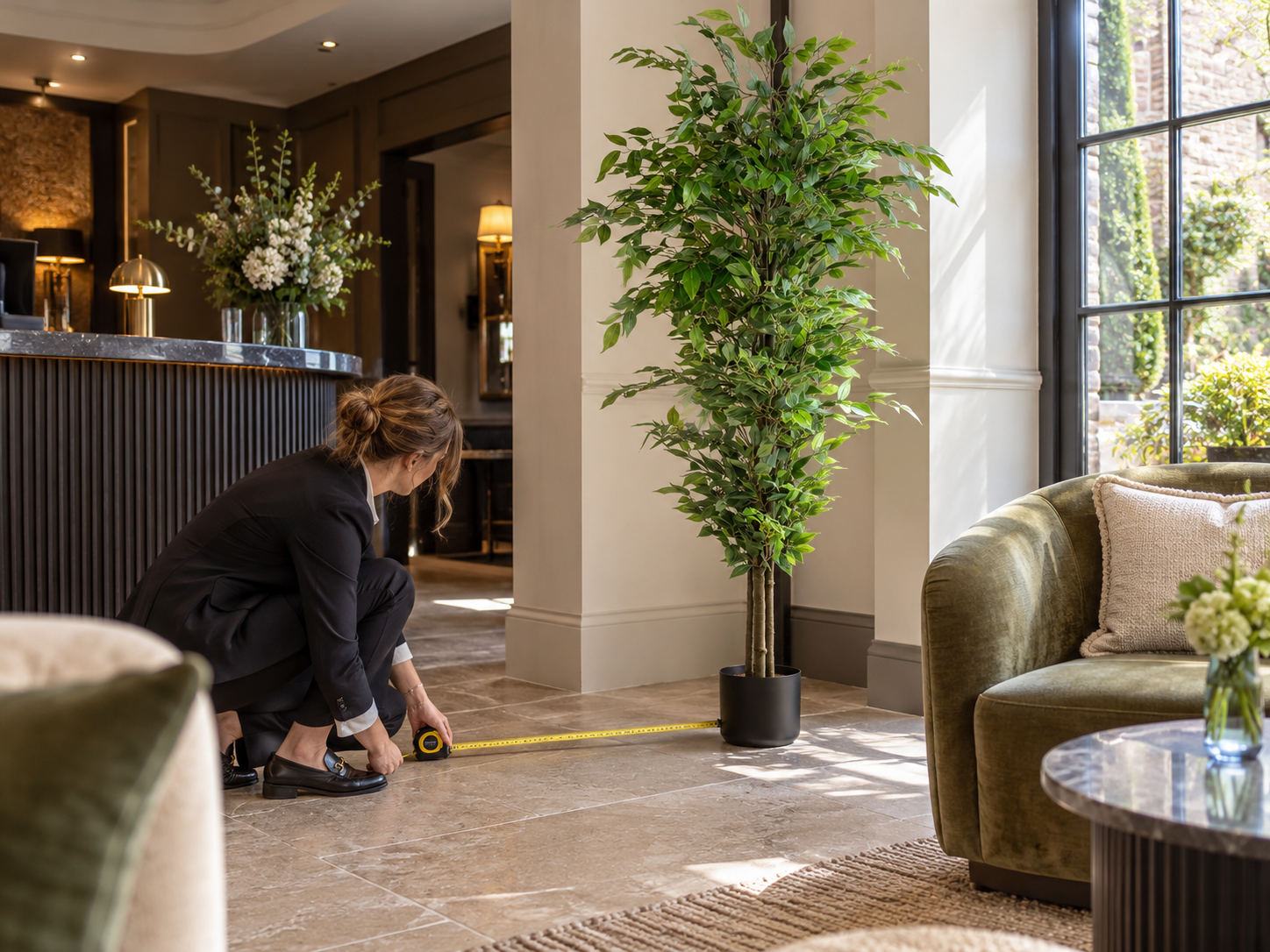 Hotel operator measuring the floor area beside an artificial ficus before placing it near reception seating